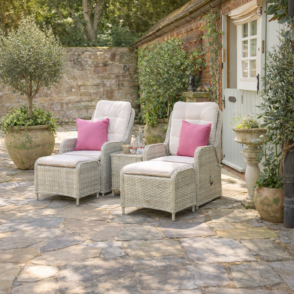 Outdoor patio furniture set with two chairs and ottoman on a stone patio, surrounded by potted plants and a brick wall.