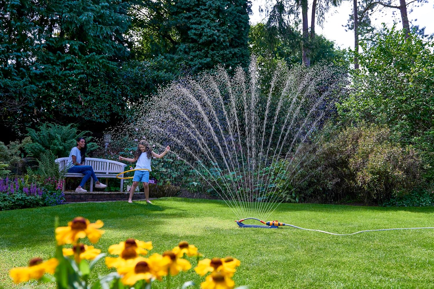 Sprinkler spraying water in a garden with people watching