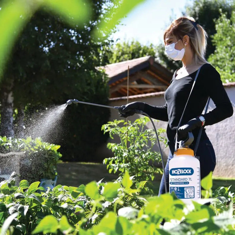 Person using a garden sprayer with a brand logo in a garden setting
