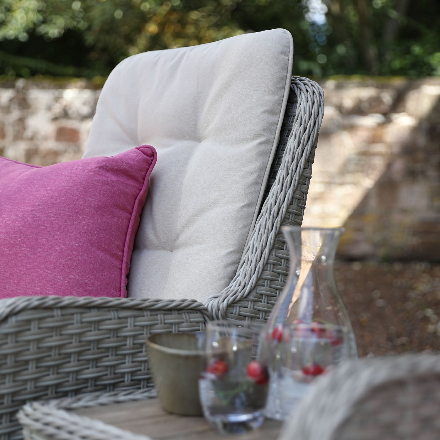 Outdoor chair with cushions and a table with glasses and a carafe in a garden setting